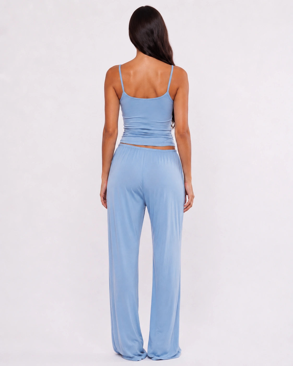 A woman shown from the back wearing a light blue two-piece lounge set consisting of a spaghetti-strap crop top and matching wide-leg pants, set against a plain white studio background.