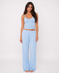A woman shown from the front wearing a light blue two-piece lounge set consisting of a spaghetti-strap crop top and matching wide-leg pants, set against a plain white studio background.