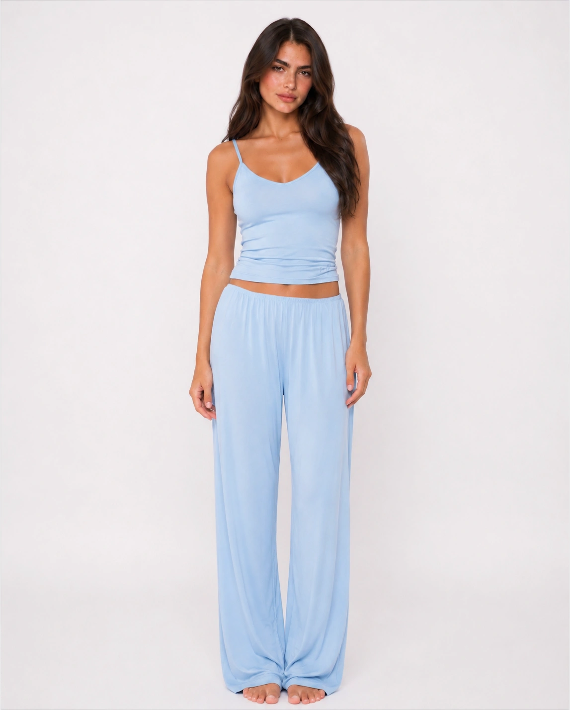 A woman shown from the front wearing a light blue two-piece lounge set consisting of a spaghetti-strap crop top and matching wide-leg pants, set against a plain white studio background.