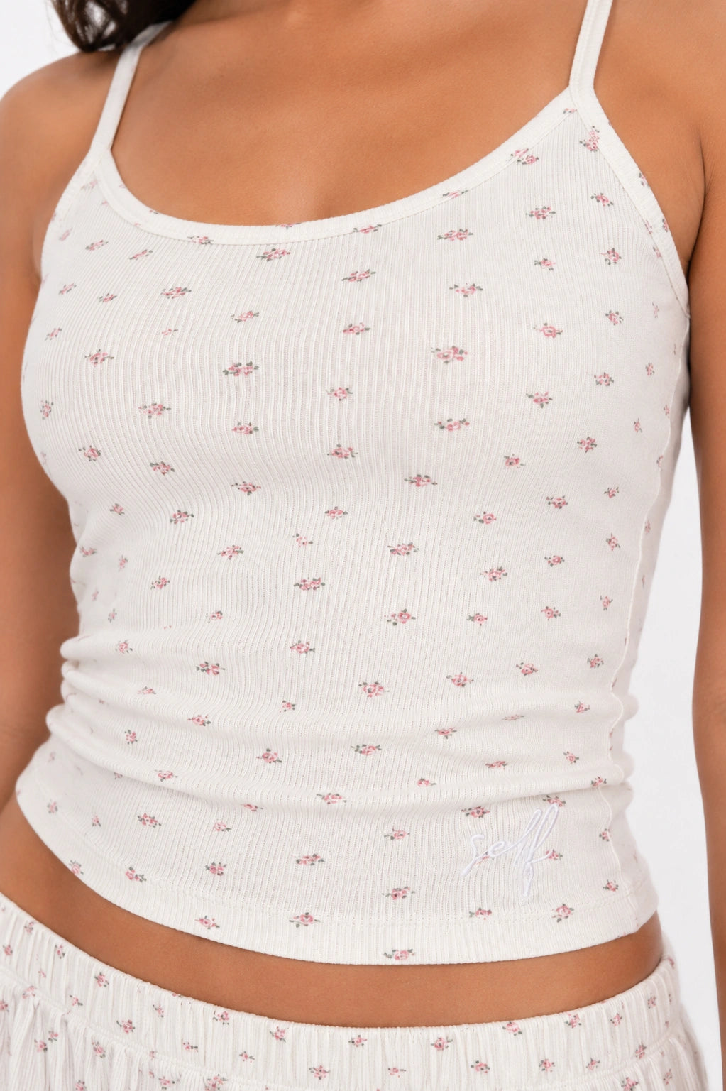 White ribbed tank top with subtle pink floral pattern worn by a person.