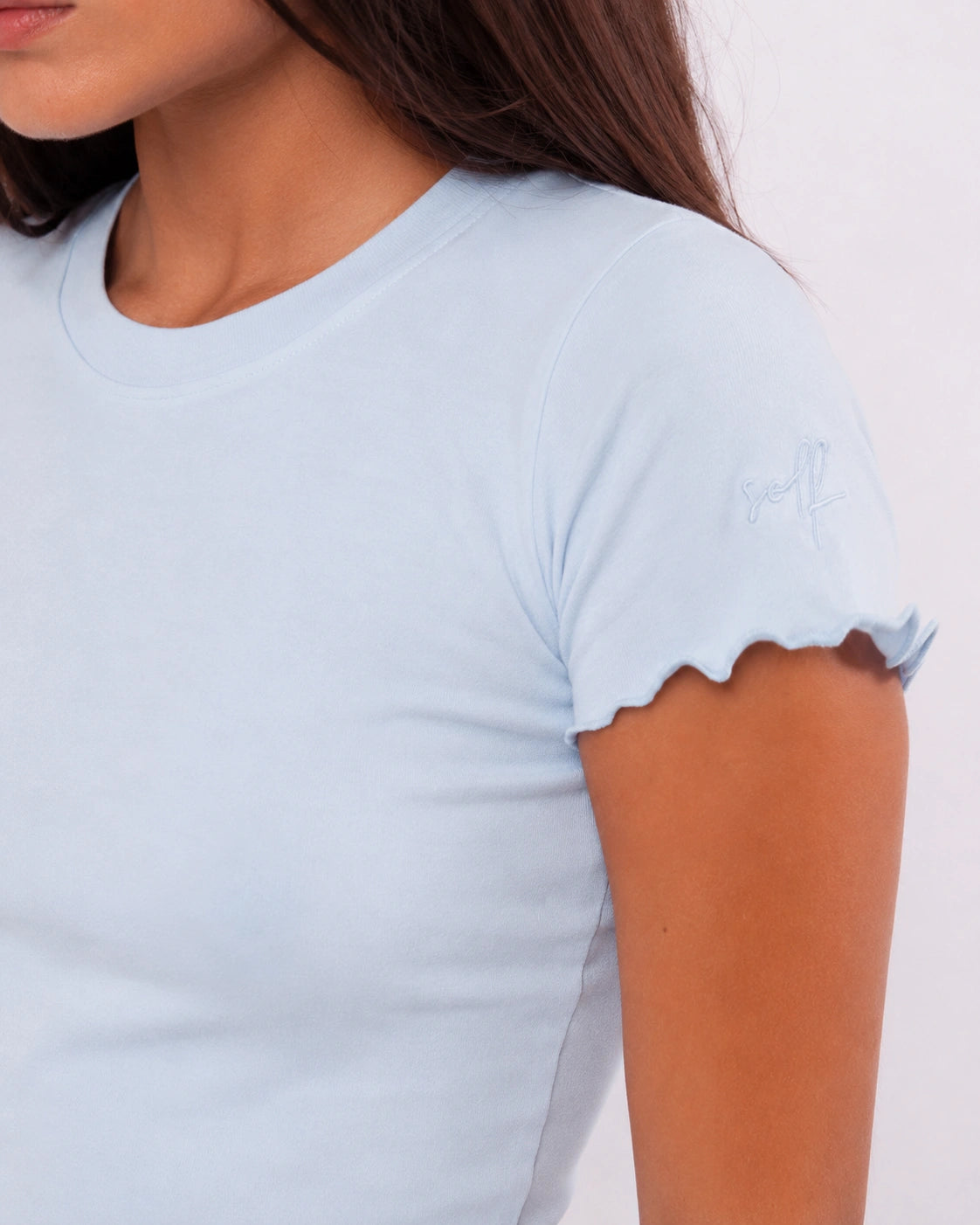 Light blue t-shirt with scalloped sleeves worn by a person on a white background