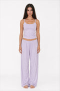 Woman wearing a light purple tank top and wide-leg pants on a white background