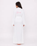 A woman viewed from the back wearing a long white robe with a matching waist belt and pink cursive 'Bride' text on the back, against a plain light background.