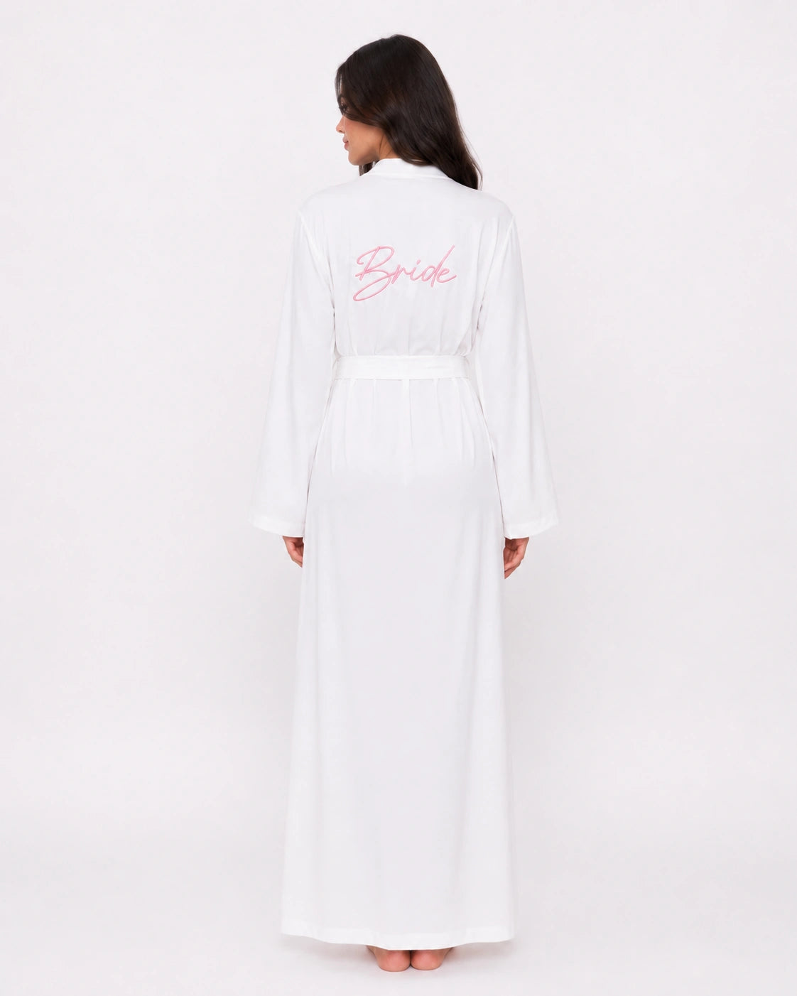 A woman viewed from the back wearing a long white robe with a matching waist belt and pink cursive 'Bride' text on the back, against a plain light background.