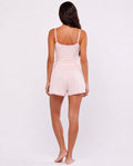 A woman viewed from behind wearing a light pink two-piece lounge set consisting of a spaghetti-strap camisole top and matching shorts, set against a plain white studio background.