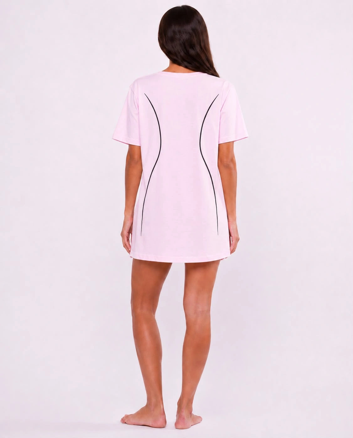 A woman viewed from behind wearing a light pink short-sleeve t-shirt dress with black curved line details on the back, standing against a plain white studio background.