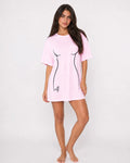 A woman modeling a light pink oversized t-shirt dress with a black line-art graphic of a torso on the front, set against a plain white studio background.