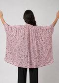 Person wearing a pink patterned shirt with arms outstretched on a plain background