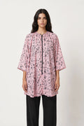 Woman wearing a pink patterned shirt with black pants on a white background