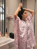 Woman wearing a pink patterned shirt with black pants on a white background