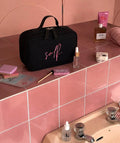 A black cosmetic bag with pink script lettering reading 'self.' 