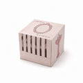 Square pink box with a design on top and striped pattern below, on a white background