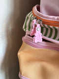 Close-up of a pastel-colored zippered bag with a pink bunny-shaped zipper pull, featuring a peach-yellow body, a pink-and-white striped section, and an orange zipper.