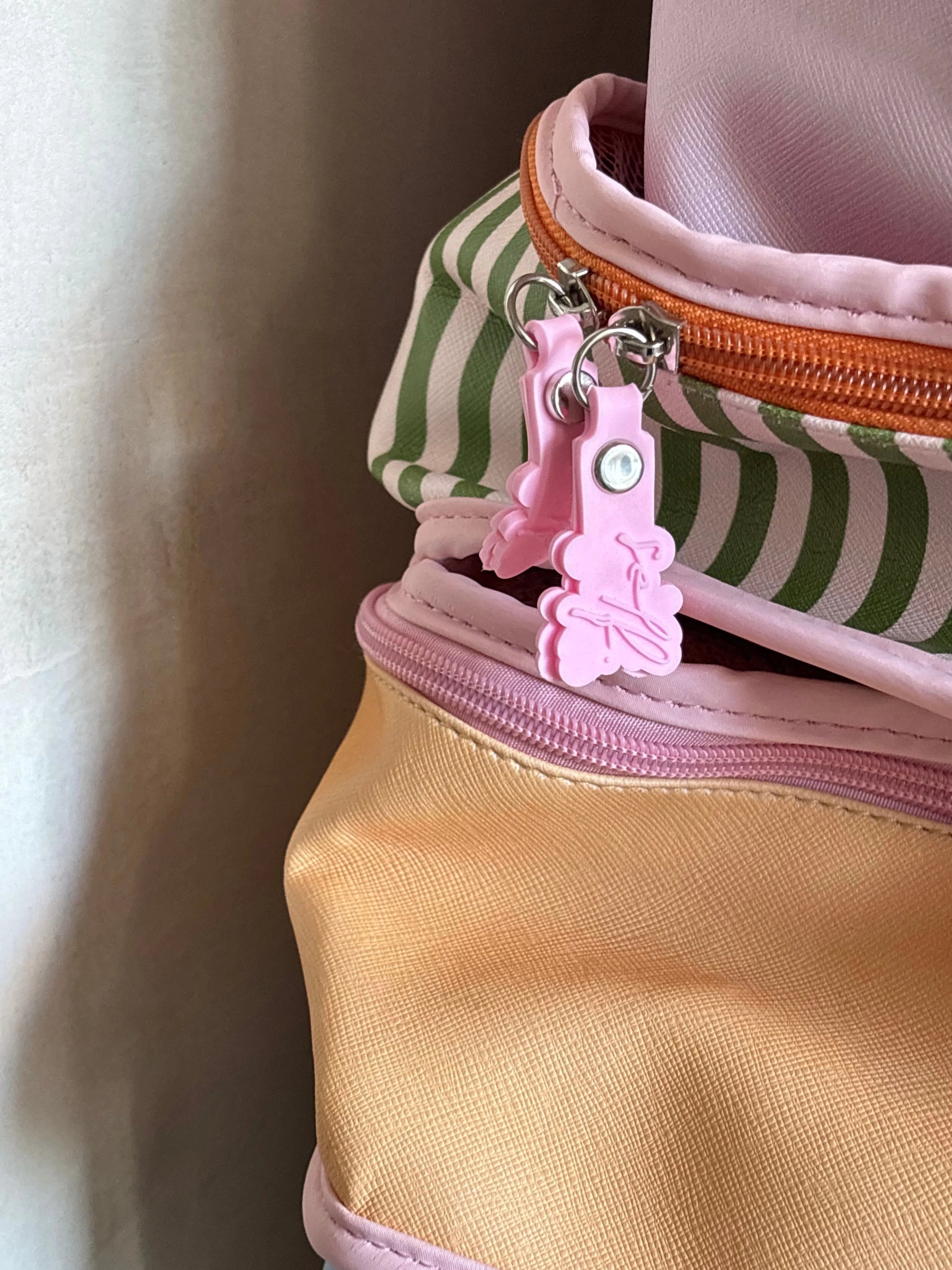 Close-up of a pastel-colored zippered bag with a pink bunny-shaped zipper pull, featuring a peach-yellow body, a pink-and-white striped section, and an orange zipper.