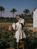 Woman in a robe holding a basket in a field with palm trees in the background